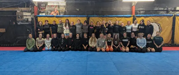 More than forty women lined up together on the mats in front of the cage