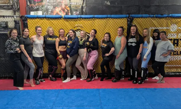 Women standing arm in arm in front of the cage at a Women of Combat event