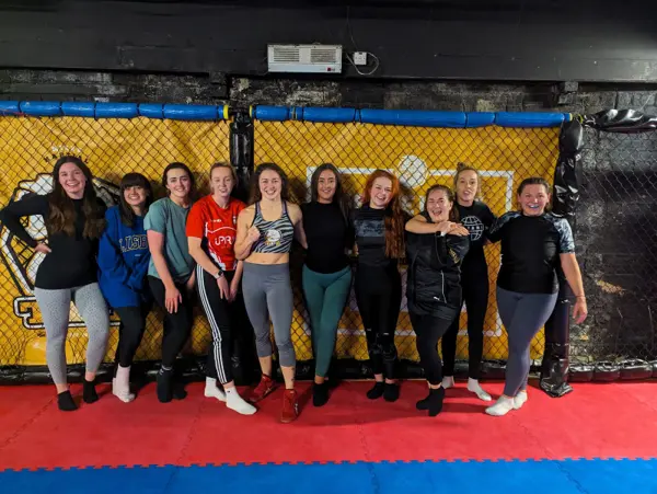 A group of women lined up arm in arm in front of a yellow cage after training