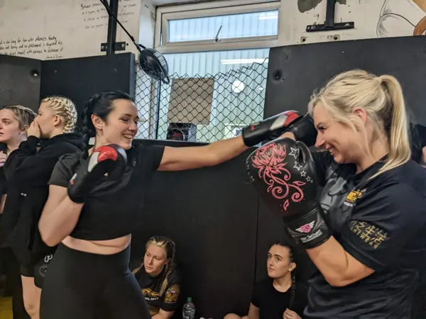 Two women smiling while drilling punches on pads