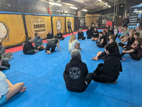 Women sitting in a circle on the mats listening to a coach at a seminar