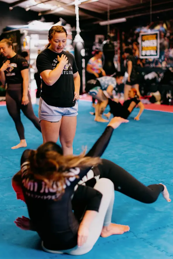 A woman completing a takedown drill on the mats while others watch