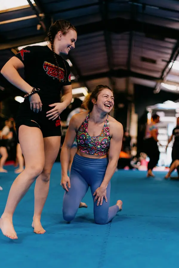 Two women laughing together between wrestling drills