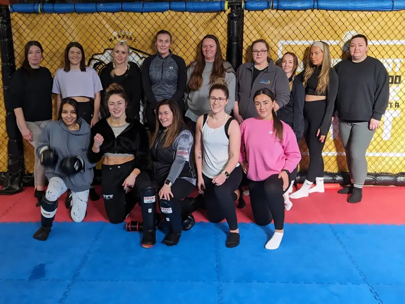 A group of women smiling together on the mats after a Women of Combat session