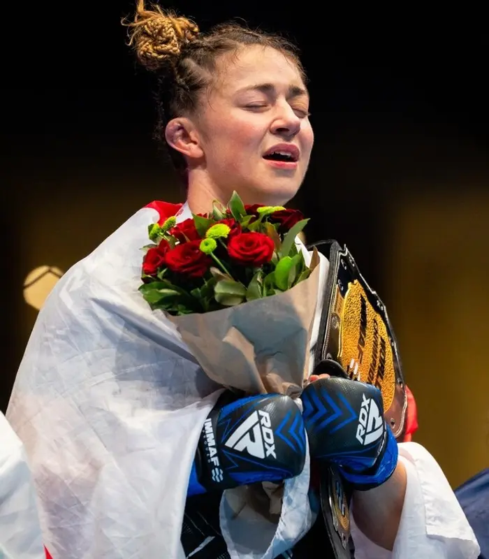Katrina Fisher on the podium with her championship belt and flowers, wrapped in the England flag