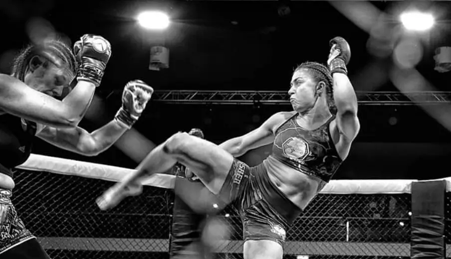 Katrina Fisher throwing a high kick during an MMA fight in the cage